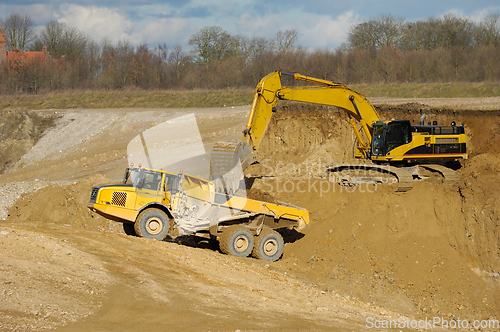 Image of Yellow dump trucks and excavator are working in gravel pit