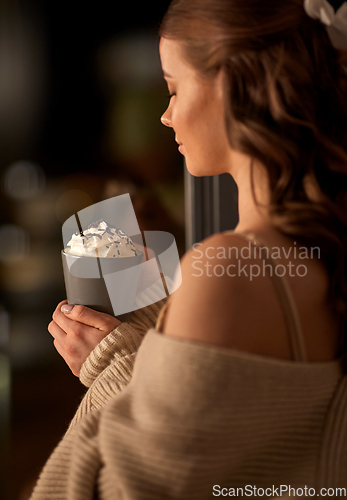 Image of woman holding mug with whipped cream at night