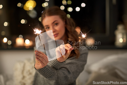 Image of happy young woman with sparklers in bed at home