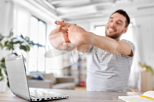 Image of happy man with laptop stretching at home office