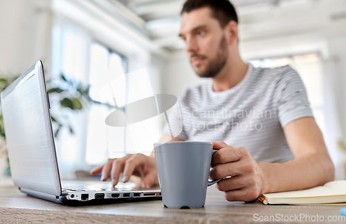 Image of man with laptop drinking coffee at home office