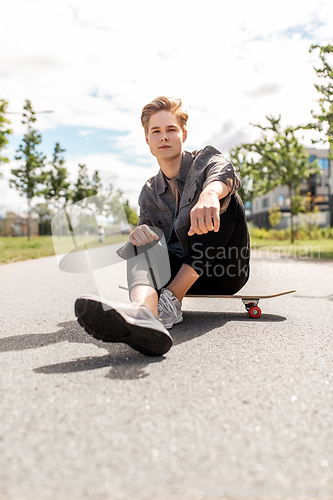 Image of teenage boy sitting on skateboard on city street