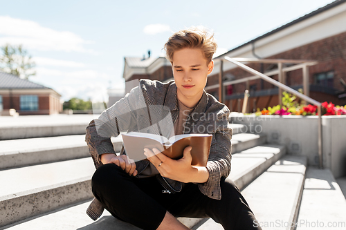 Image of young man or teenage boy reading book in city