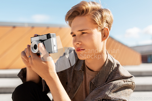 Image of young man with camera photographing in city