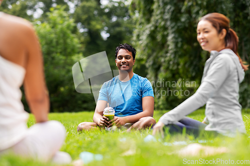 Image of group of people sitting on yoga mats at park