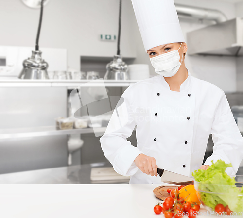 Image of female chef in mask cutting vegetables at kitchen