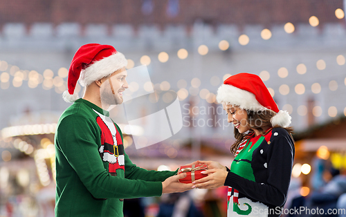 Image of happy couple in christmas sweaters with gift box