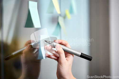 Image of hand with marker and sticker on glass at office