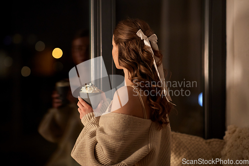 Image of woman holding mug with whipped cream at night