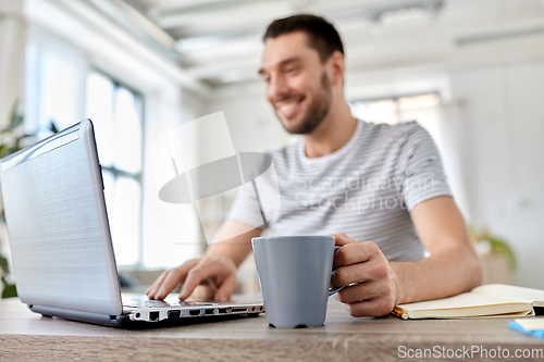 Image of happy man with laptop drinking coffee at home