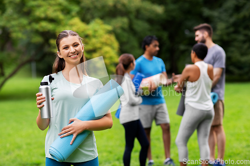 Image of smiling woman with yoga mat and bottle at park