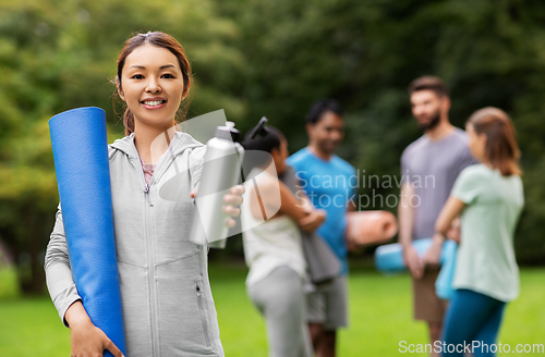 Image of smiling woman with yoga mat and bottle at park