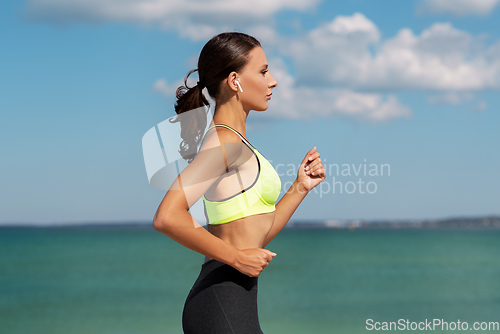 Image of woman with wireless earphones running at seaside