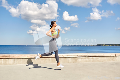 Image of young woman running along sea promenade