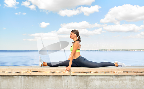 Image of young woman doing full split at seaside