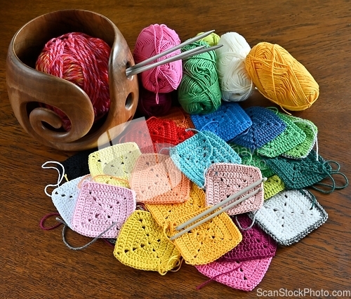 Image of colorful knitted squares, skeins of wool and a wooden yarn bowl