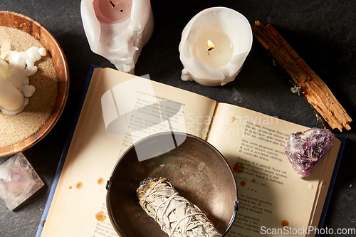 Image of magic book, sage, burning candles and ritual staff