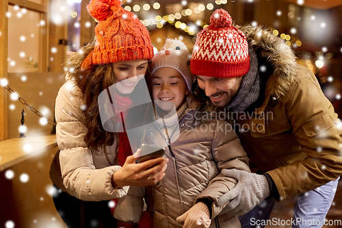 Image of happy family with smartphone at christmas market