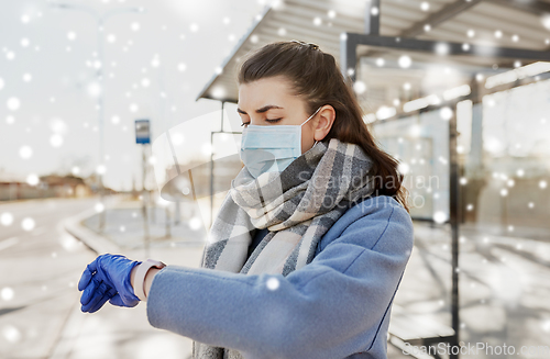 Image of woman in mask looking at wristwatch at bus stop