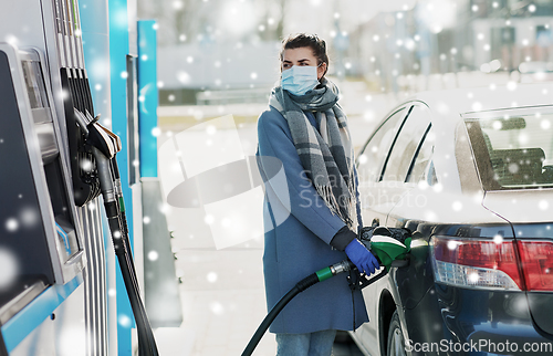 Image of woman in mask filling her car at gas station