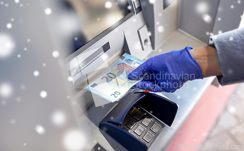 Image of hand in medical glove with money at atm machine