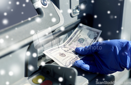 Image of hand in medical glove with money at atm machine