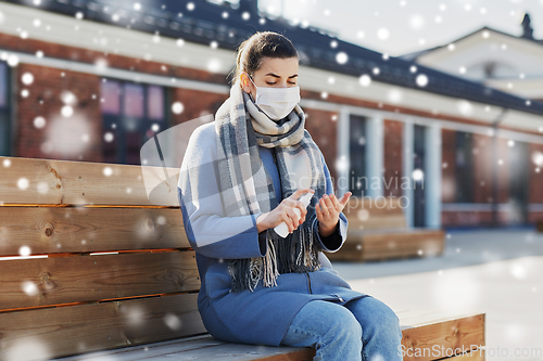 Image of woman in mask spraying hand sanitizer outdoors