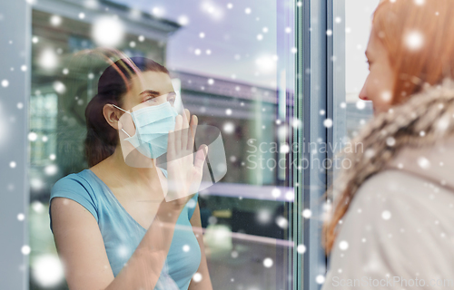 Image of ill woman in mask looking at friend through window