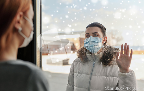 Image of woman in mask looking to friend through window