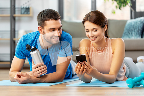 Image of happy couple with smartphone after sports at home