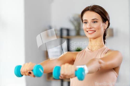 Image of happy woman with dumbbells exercising at home