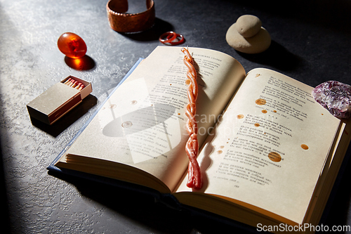 Image of magic book, wax candle, matches and gem stones