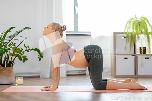 Image of happy pregnant woman doing yoga cow pose at home