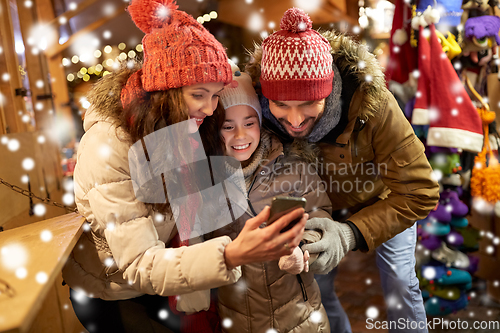 Image of happy family with smartphone at christmas market