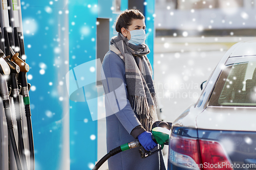 Image of woman in mask filling her car at gas station