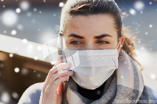 Image of woman in face mask calling on smartphone in city