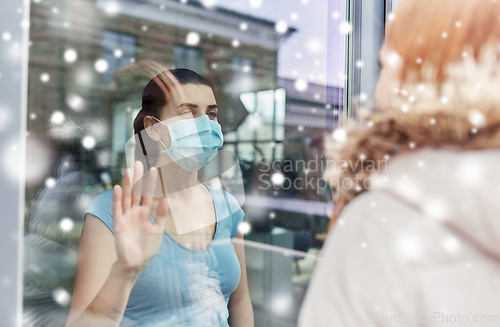 Image of ill woman in mask looking at friend through window