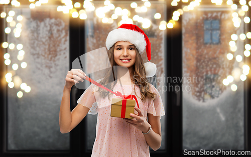 Image of teenage girl in santa hat opening christmas gift