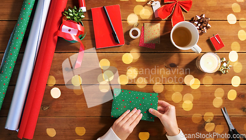 Image of hands wrapping christmas gift into paper at home