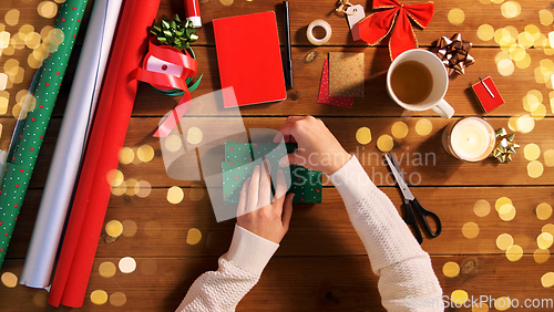 Image of hands wrapping christmas gift into paper at home