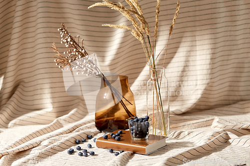 Image of cup of blueberry, book and dried flowers in vases