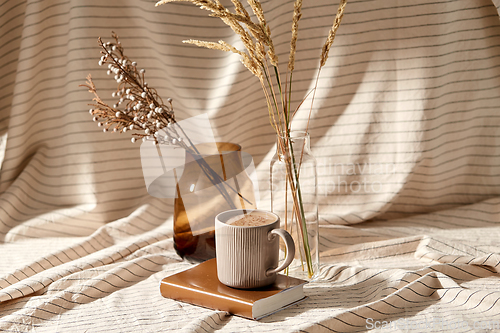 Image of cup of coffee on book and dried flowers in vases