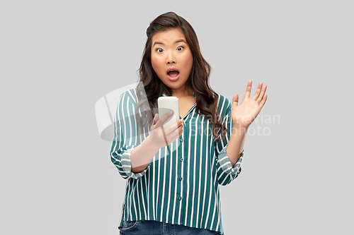 Image of surprised asian woman using smartphone