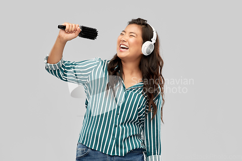 Image of asian woman in headphones with hairbrush singing