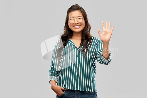 Image of happy asian woman in glasses waving hand