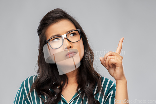 Image of worried asian woman in glasses pointing finger up