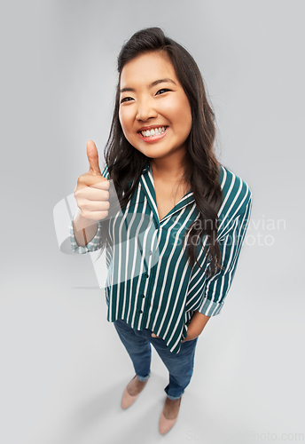 Image of happy asian woman showing thumbs up over grey