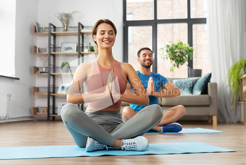 Image of happy couple meditating in yoga lotus pose at home