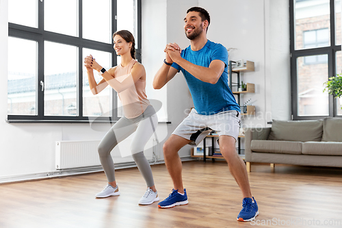 Image of happy couple exercising and doing squats at home