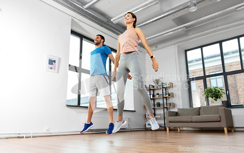 Image of happy couple exercising and jumping at home